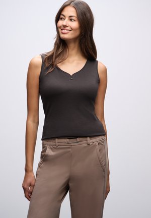 Top sans manches noir avec un col en V et deux boutons, associé à un pantalon beige avec des poches latérales et une texture lisse.