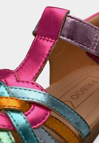 Κοντινό πλάνο διαφορετικών έγχρωμων μεταλλικών λουριών δερμάτινων σανδαλιών σε ροζ, μοβ, μπλε, πορτοκαλί και πράσινο με ορατή ραφή και ταμπά εσωτερική σόλα.