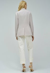 Blazer grigio chiaro con vestibilità sartoriale, spacco posteriore e dettagli con bottoni. Abbinato a pantaloni bianchi con risvolto e tacchi leggeri con cinturini.