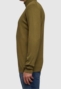 Olivgrüner, langärmeliger Rollkragenpullover aus weichem Strickstoff, mit gerippten Bündchen und Saum, kombiniert mit engen blauen Jeans.