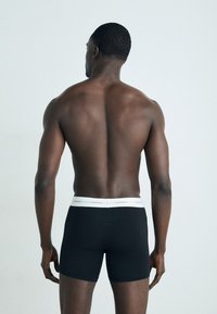 Boxer neri con una fascia bianca di Calvin Klein, caratterizzati da una texture liscia e un design aderente. Visibile la schiena del modello.