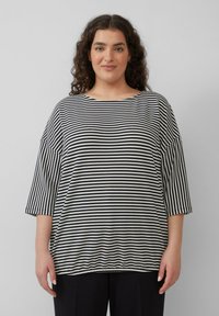 Gestreept zwart-wit oversized katoenen shirt met driekwartmouwen, brede halslijn en geribbelde textuur. Zachte stofafwerking.