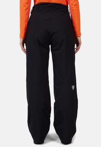 Pantaloni outdoor neri realizzati in materiale resistente, con una vestibilità rilassata e un logo sul lato sinistro, progettati per un uso attivo.