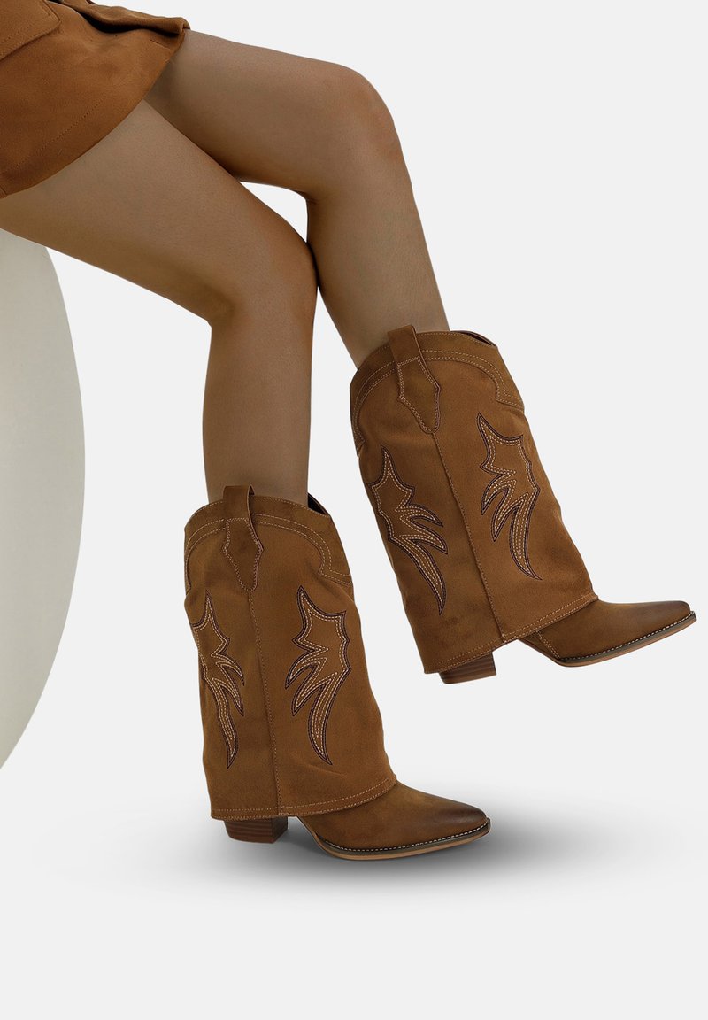 Botas de vaquero de ante marrón con puntas afiladas, tacones angulados y bordados en contraste. Presentan costuras decorativas en el caño.