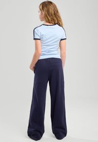 Vaaleansininen istuva t-paita tummansinisin yksityiskohdin, yhdistettynä löysiin tummansinisiin housuihin, joissa on takatasku, sileä pinta ja rento muotoilu.