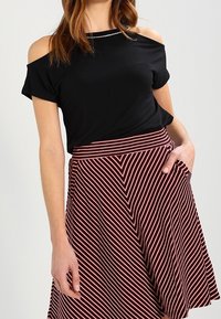 Černý top bez ramínek doplněný červeno-bílou pruhovanou sukní. Sukně má diagonální pruhy a boční kapsy.