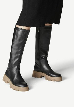 Bottes noires en cuir, montantes jusqu'aux genoux, avec une semelle épaisse beige, dotées d'une fermeture éclair sur le côté et d'une texture lisse.