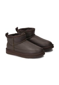Botines de cuero marrón con acabado texturizado, forro de piel suave, tacón reforzado y dos tiradores. Presenta detalles de costura en contraste.