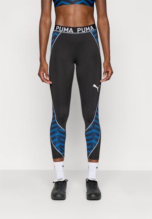 Leggings negros con patrones geométricos azules, cinturilla elástica con el logo "PUMA" y emblema blanco de la marca cerca del tobillo.
