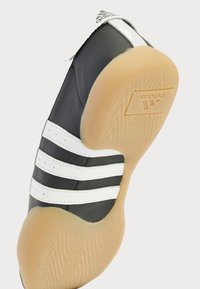 Black leather athletic shoe with white stripes, rubber gum sole, rounded toe, and Adidas logo on the heel. Textured sole for traction.