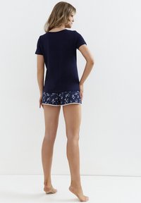 Granatowa bawełniana koszulka z krótkim rękawem w połączeniu z granatowymi szortami w kwiatowy wzór, które mają białe wykończenie. Model stoi boso, widoczny od tyłu.