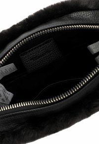 Interno di una borsa in pelle nera con un rivestimento testurizzato e dettagli in pelliccia. Dettagli della cerniera e etichette di cura visibili all'interno.
