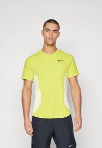 Limegrøn atletisk skjorte med korte ærmer, sort Nike-logo på brystet, kontrasterende hvide sidepaneler og rund halsudskæring.