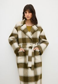 Cappotto a quadri realizzato in morbido tessuto verde e bianco, con vita aderente, collo oversize e tasche frontali.