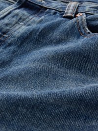 Κοντινό πλάνο από μπλε τζιν ύφασμα με ορατή πορτοκαλί ραφή και θηλιά ζώνης σε ένα ζευγάρι τζιν.