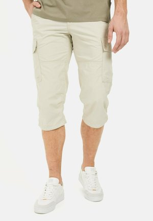 Beige Cargo-Shorts mit knielangem Schnitt, zwei Seitentaschen und entspannter Passform; kombiniert mit weißen Sneakers.
