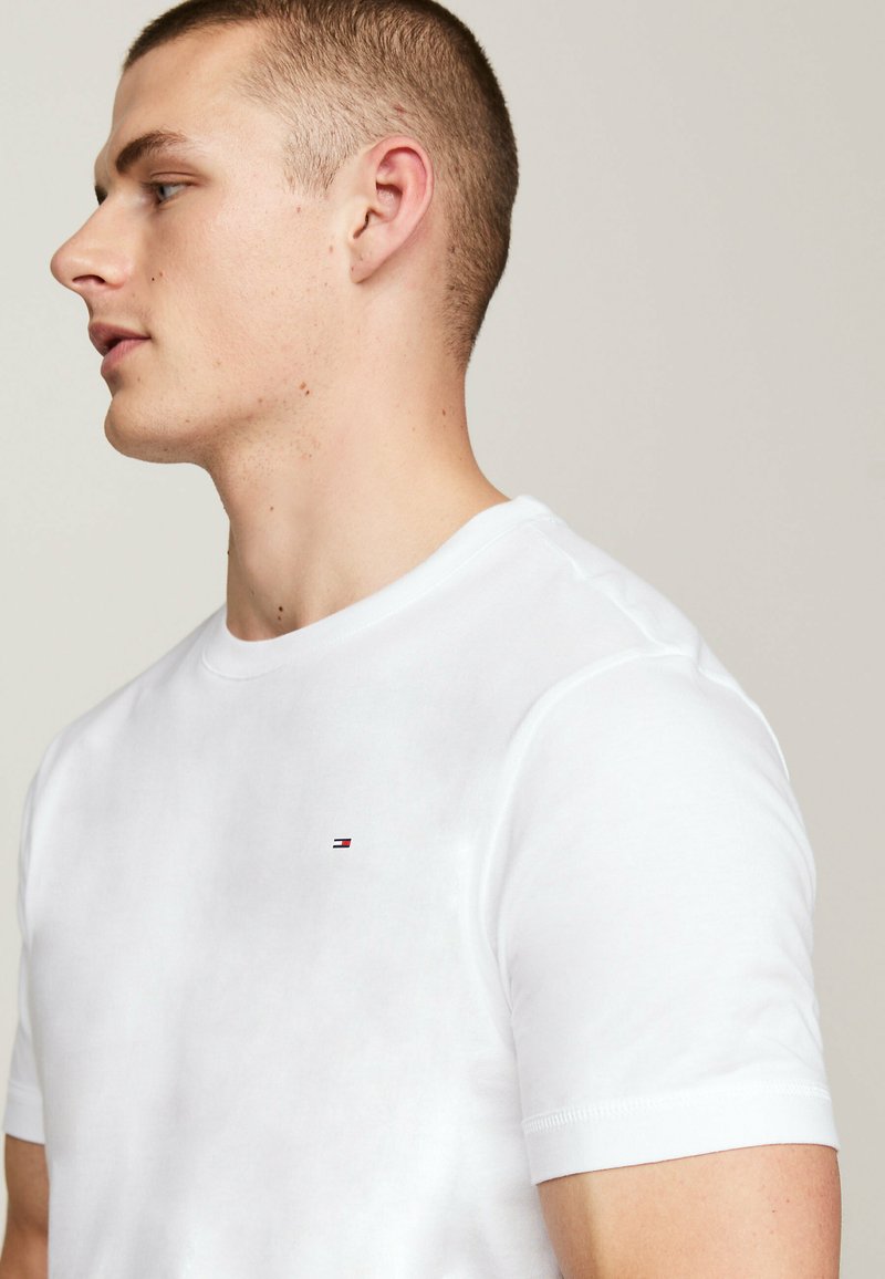 Witte katoenen t-shirt met een ronde hals, korte mouwen en een klein geborduurd logo op de borst. Glad textuur, eenvoudig ontwerp.