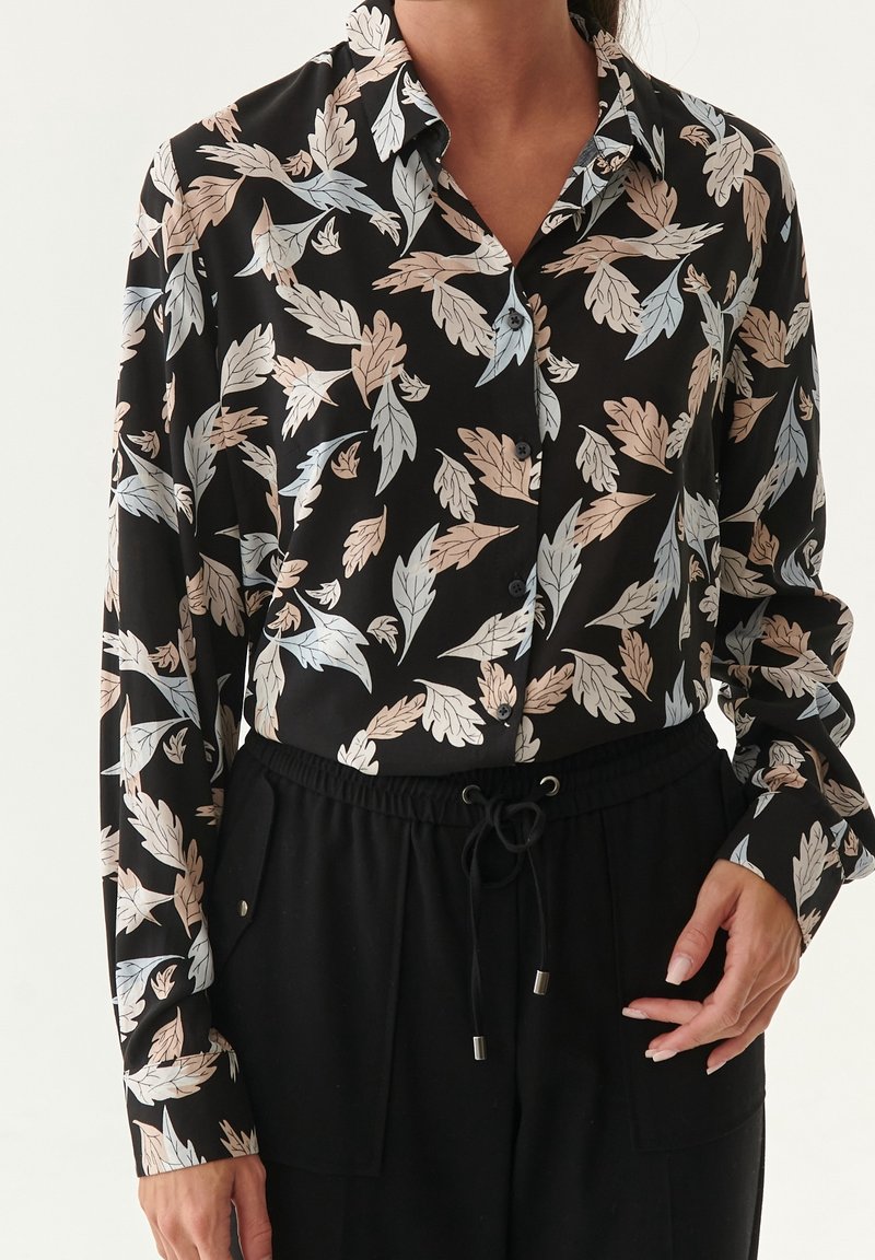 Chemise noire à boutons avec motifs de feuilles beige clair et gris, associée à un pantalon noir à cordon, vue du cou aux hanches.