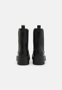 Bottines en cuir noir avec une texture lisse, des panneaux latéraux élastiques et une semelle en caoutchouc épaisse avec des crampons prononcés.