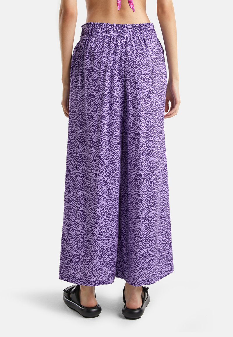 Pantalons en large jambe à imprimé léopard violet avec une taille élastique. Tissu léger qui tombe jusqu'aux chevilles, associés à des chaussures noires à enfiler.