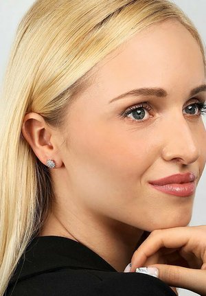 Funkelnde silberne Ohrstecker mit floralem Design, die mehrere kleine Edelsteine und eine polierte Oberfläche aufweisen, getragen im Ohr eines Models.