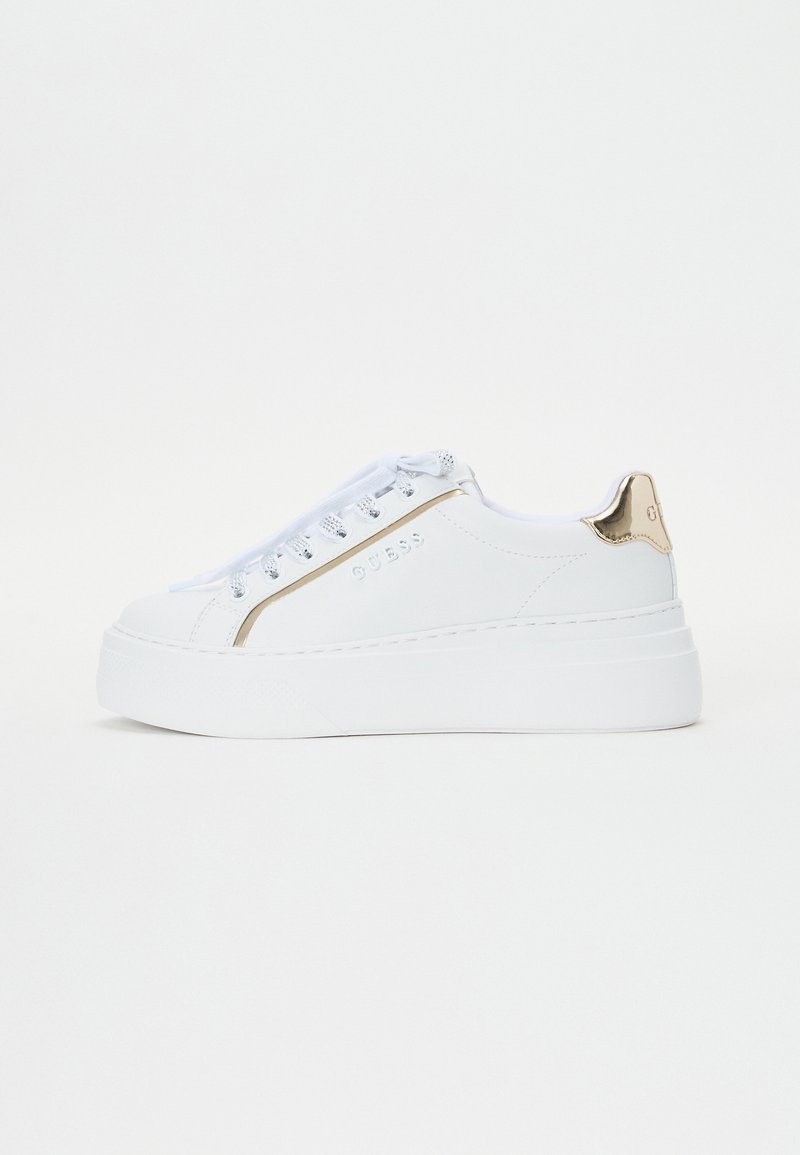 Sneakers bianchi con piattaforma e finitura liscia, dotati di un accento metallic oro, suola testurizzata e design con lacci. Nome del marchio "GUESS" visibile.