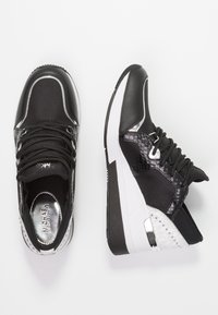 Svartvita sportskor med en texturerad svart ovandel, slank design, silverdetaljer och en dämpad sula. Snören ingår.