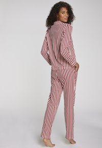 Vrouw met krullend haar in een rood-wit gestreepte pyjama, staat blootvoets en kijkt over haar schouder.
