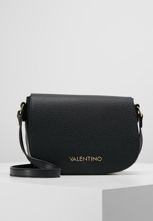 Sort tekstureret læder Valentino crossbody taske med klaplukning og guld logo bogstaver foran, hvilende på en hvid overflade.