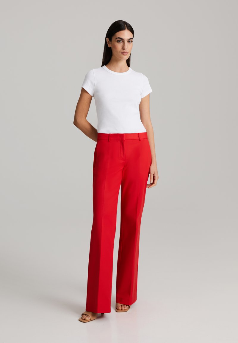 Tricou alb cu mânecă scurtă, asortat cu pantaloni roșii cu talie înaltă. Pantalonii au o tăietură dreaptă, cu o textură netedă și linii de pliuri subtile.