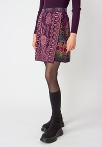 Knee-length purple skirt with floral and geometric patterns in pink and green. Smooth texture, complemented by a solid colored waistband.