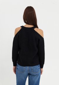 Pull noir en maille avec épaules ouvertes et texture côtelée, associé à un jean bleu clair taille haute.