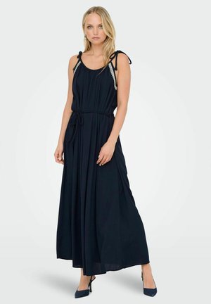 Navy blue maxi dress with shoulder ties, pleated texture, and a cinched waist. Features decorative trim along the neckline.