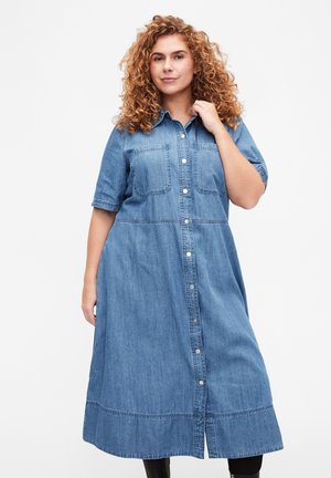 Abito camicia in denim di colore azzurro chiaro, con maniche corte, chiusura con bottoni frontale, due tasche sul petto e un orlo caratterizzato da delicate cuciture decorative.