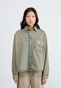 Light blue, oversized denim shirt with a front pocket, silver buttons, and a collar. Features a faded, textured finish.
