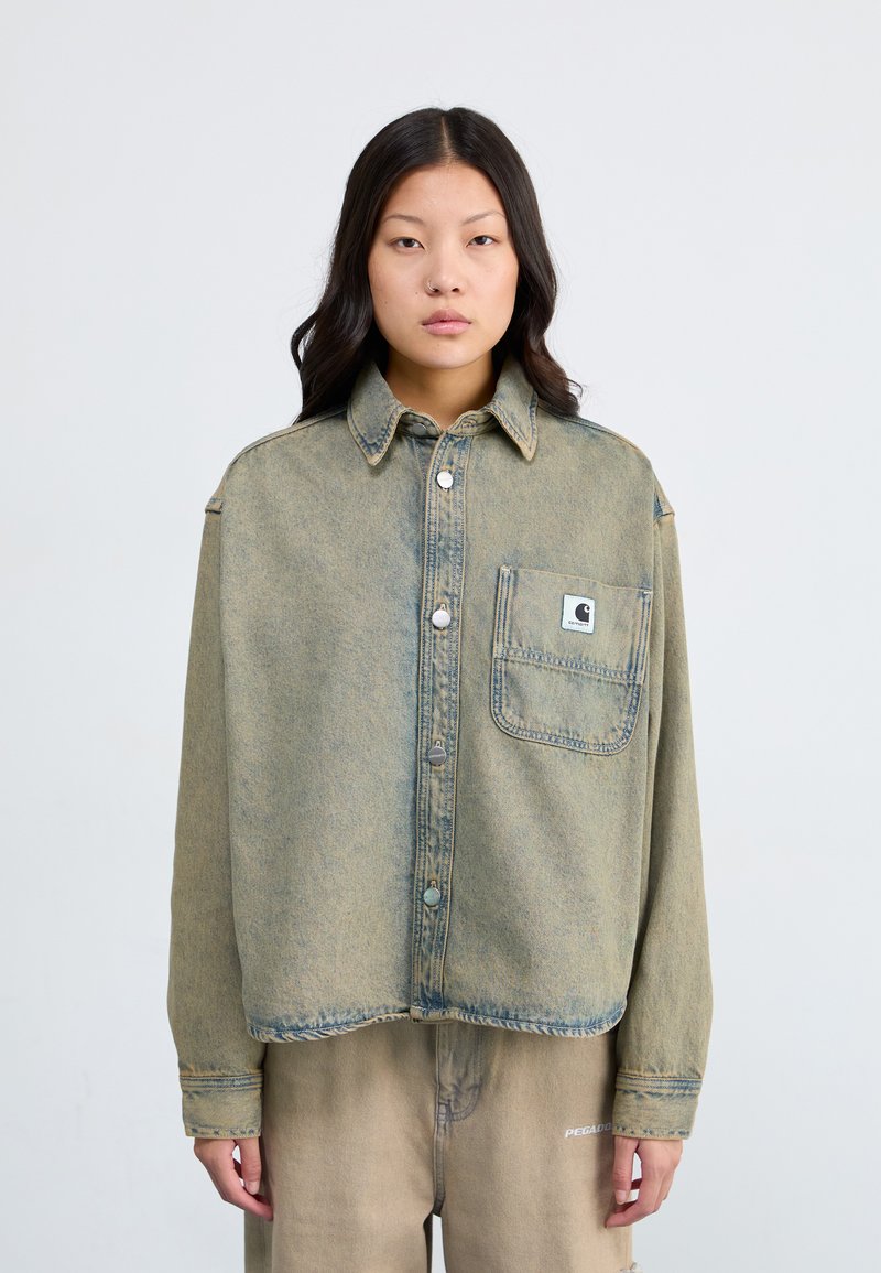 Light blue, oversized denim shirt with a front pocket, silver buttons, and a collar. Features a faded, textured finish.