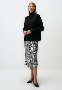 Pull en tricot noir avec un col roulé montant, associé à une jupe midi rayée noir et blanc façon zèbre. Le modèle porte des talons aiguilles noirs.