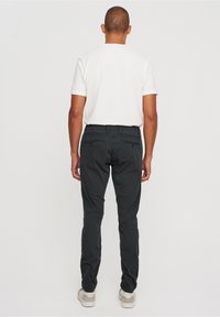 Black trousers made of cotton, featuring a slim-fit design, two back pockets, and subtle stitching details, paired with a white t-shirt.