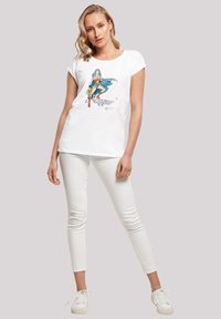 White cotton t-shirt featuring a colorful superhero graphic, round neck, short sleeves, and relaxed fit. Paired with white skinny jeans.