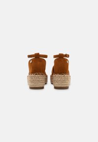 Brown suede platform sandals with ankle straps and braided jute detail around the sole. Smooth texture with a rounded design.