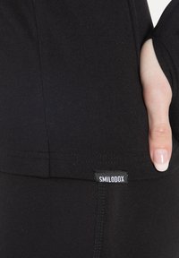 Black leggings with a smooth texture, a pocket at the side, and a small white label displaying "SMILODOX" near the hem.