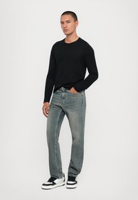 Black long-sleeve shirt, light gray jeans with a straight cut, and black and white sneakers. Simple design with a classic fit.