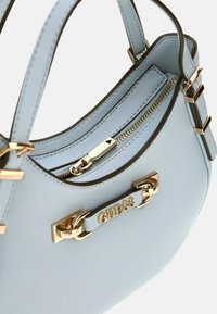 Borsa a mano in pelle blu chiaro con una forma strutturata, hardware color oro, tasca con zip e dettaglio logo sulla parte anteriore.