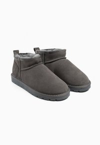 Botas de tobillo de ante gris con un suave forro de piel, puntera redondeada y suela de goma; costuras mínimas y una lengüeta en la parte posterior para facilitar su puesta.