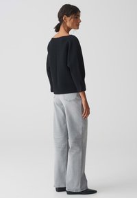Haut noir texturé avec un col bateau et des manches larges, assorti à un jean large gris clair et des bottines noires.