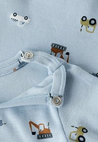 Jasnoniebieska tkanina z nadrukiem pojazdów budowlanych w odcieniach pomarańczowym, żółtym i czarnym. Posiada zatrzaski przy dekolcie, co ułatwia zakładanie.