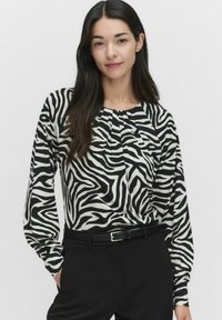 Musta-valkoinen zebra-raidoitettu pitkähihainen paita, jossa on pyöreä pääntie ja poimutustyyny. Yhdistetty mustiin housuihin ja vyöhön.
