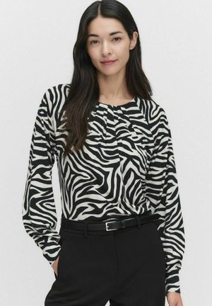 Zebrapasten zwart-wit gestreepte blouse met lange mouwen, voorzien van een ronde halslijn en geplooide details. G gedragen met zwarte broek en een riem.