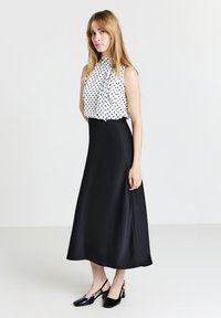 Gonna di raso nera abbinata a un top senza maniche bianco con pois neri. Dettagli notevoli includono un collo alto e una silhouette fluida.
