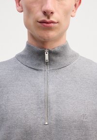 Grauer Reißverschluss-Sweatshirt mit hohem Kragen, gerippter Textur und kleinem gesticktem Logo auf der linken Brust.